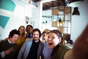 Young adult coworkers laughing while taking selfie in creative office