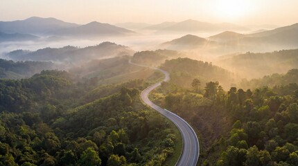 Aerial view of winding road through lush green mountains shrouded in misty morning light