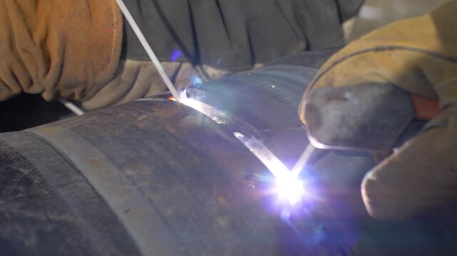 Welder using stick welding process on metal pipe on construction site.