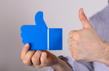 Hand holding blue like symbol, thumbs up gesture.  Positive feedback, approval, social media concept.
