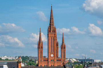 Fototapeta premium A telephoto shot of Wiesbaden Evangelical Market church on a clear spring day, bathed in sunlight against a backdrop of blue skies and white clouds.