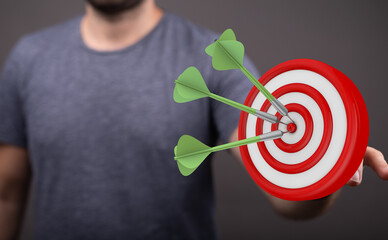 A close up of a man holding a dart board with darts hitting the bullseye representing a goal, success, and strategy.
