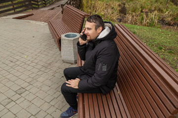 man in a city park with a phone wearing a black jacket in cloudy autumn weather