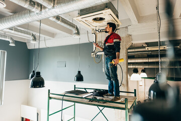 Worker installs HVAC unit in modern building interior during daytime renovation project