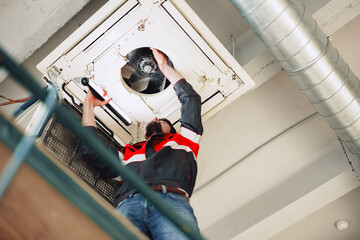 Technician repairs ventilation system in commercial building during daylight hours