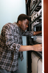 Fototapeta premium Young technician troubleshooting network equipment in a server room during daylight hours