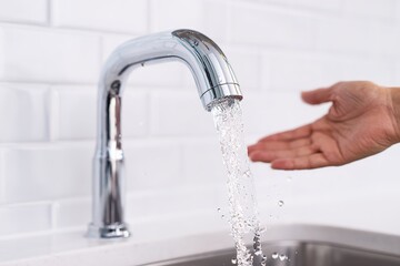 Water flows from a modern kitchen faucet as a person holds their hand under the stream in a clean kitchen space