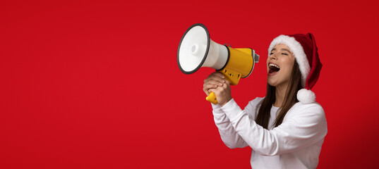 A woman wearing a Santa hat enthusiastically shouts into a yellow megaphone. She stands against a...