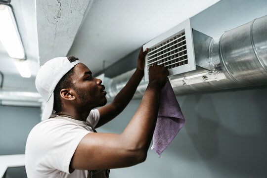 Man cleaning air vent in basement space during daylight hours for better air quality and system maintenance