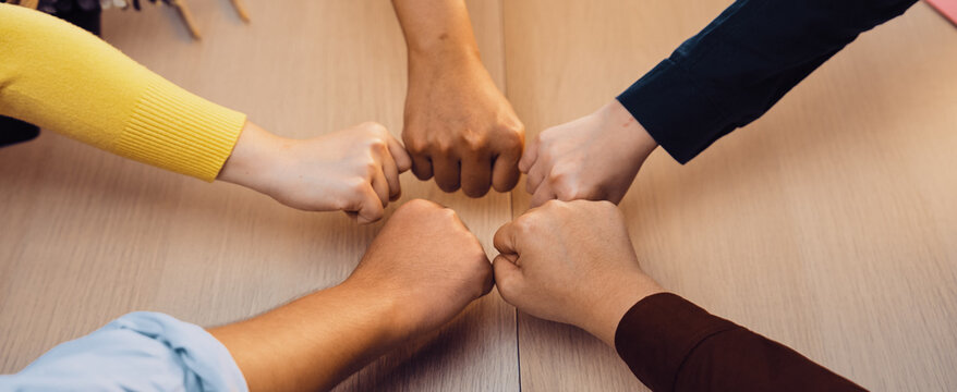 A vibrant scene depicting diverse hands engaging in a fist bump over a wooden table, illustrating teamwork, collaboration, and camaraderie in a modern office setting. SACTR - Powered by Adobe