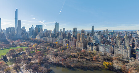 Aerial view of Central Park's autumnal hues meet the towering skyscrapers under a clear sky, a vibrant contrast of nature and urbanity, Manhattan, New York, United States.