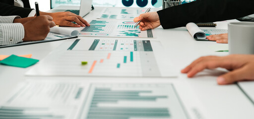 A group of business professionals collaborates during a meeting, analyzing diverse financial charts and reports while utilizing modern technology in a sleek office setting. SACTR