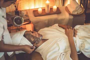 Serene ambiance of spa salon, woman customer indulges in rejuvenating with charcoal face cream massage with warm lighting candle. Facial skin treatment and beauty care concept. Quiescent