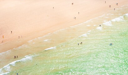 Aerial view of golden sands kissed by turquoise waves where people stroll and surf under the summer sun, Newquay, England, United Kingdom.