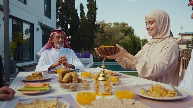 Muslim family celebrating eid al-fitr outdoors, sharing traditional dishes at a modern backyard dining table beside a swimming pool, multi-generational joy and togetherness