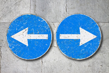 Old blue metallic arrow sign against a stone wall indicating to go left and right - concept image