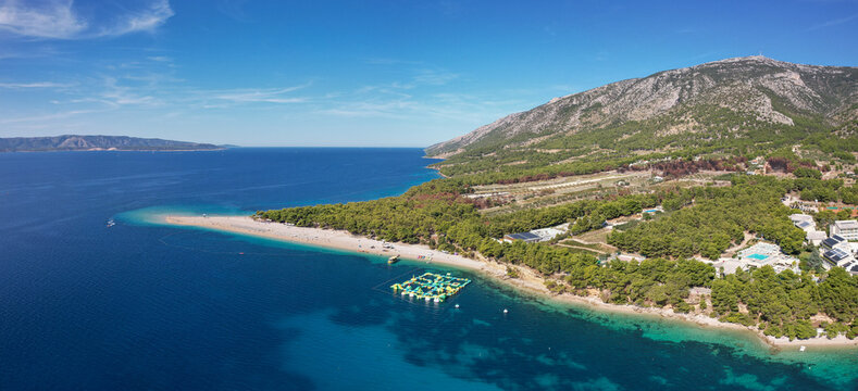 Aerial view of a golden sandspit extending into the azure sea against a backdrop of forested mountains, Bol, Croatia.