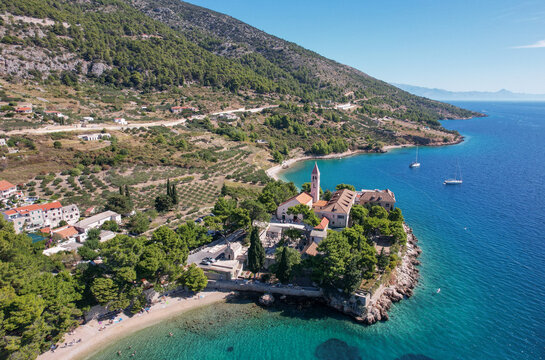 Aerial view of vibrant turquoise waters meet the rugged coastline, highlighting the historic Dominican Monastery amidst lush greenery, Bol, Split-Dalmatia County, Croatia.