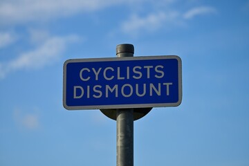 Cyclists Dismount Traffic Sign Against Blue Sky with Clouds