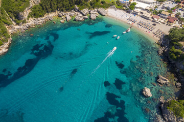 Aerial view of a boat gliding through the turquoise waters of a secluded bay near rocky cliffs and sandy beach, Corfu, Corfu, Greece.