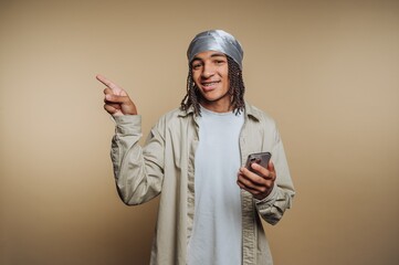 Young man with a headscarf holding a smartphone and pointing.