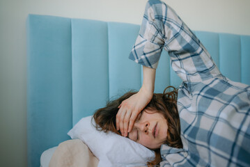 Woman lying in bed with a hand on her forehead, displaying discomfort and pain from a severe headache, fever, or chronic illness, signifying health problems and needing rest