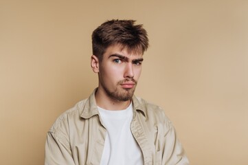 Young man with a skeptical expression against a beige background.