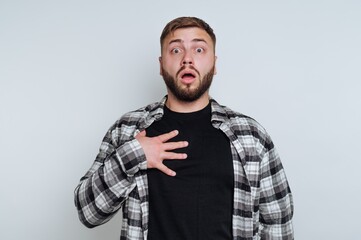 Fototapeta premium A surprised man with a beard and plaid shirt holding his chest.