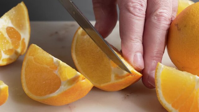 A knife slices into a halved orange on a cutting board. Close-up details show juicy pulp, rind, and white pith during food prep.