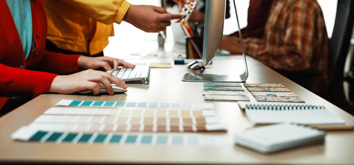 A bright modern office scene featuring creative professionals collaborating on a design project, utilizing color swatches, laptops, and desks to inspire ideas and foster teamwork. SACTR