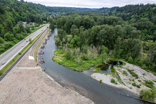 Aerial view of the Cedar River meandering through a lush green valley near a highway, the water reflecting the sky under a cloudy sky, Renton, Washington, United States.
