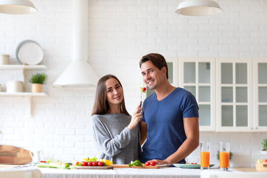 Smiling man in a blue shirt is sitting at a kitchen table with a woman in a gray shirt. Happy expression.
