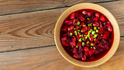 Homemade, vegan beet borscht (in Ukrainian style) topped with scallions. Rustic wooden table with copy space. 