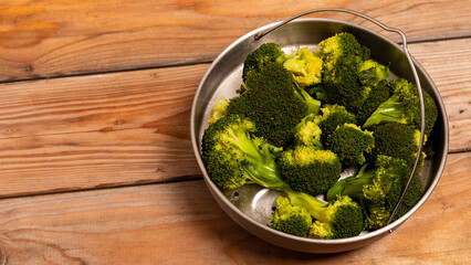 Steamed broccoli florets in a stainless steel steamer on a rustic wooden table. Healthy vegetable concept. Copy space.