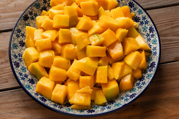 Peeled, ripe mango fruit pieces on a plate. Rustic wooden table.
