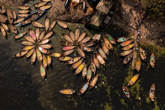 Aerial view of boats clustered together like petals of a flower on the water, beside stairs and tents, Dhaka, Dhaka Division, Bangladesh.