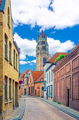 Obraz premium Bruges old town district, narrow cobblestone street, colorful buildings with brick walls in Brugge city historic center, St. Salvator's Cathedral tower, vertical view, West Flanders province, Belgium