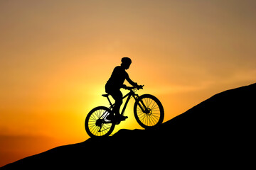 Obraz premium Silhouette of a cyclist riding uphill at sunset, embodying determination and adventure