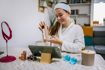 Young woman sits at home, filming a beauty vlog on her tablet and giving skincare and makeup advice.