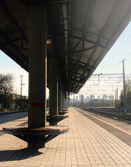 Naklejka premium Quiet train station platform with waiting area and tracks visible under bright sunlight