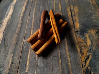 Cinnamon sticks are arranged on a rustic wooden surface, highlighting their curled, textured appearance.