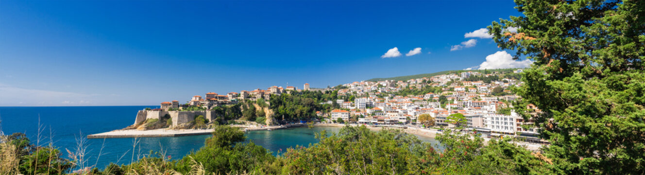Panoramic view of Ulcinj, Montenegro, featuring the historic Old Town, sandy beaches, and hillside houses overlooking the blue Adriatic Sea under a clear summer sky.