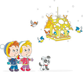 Happy little boy and girl with their puppy watching small birds merrily flying around a homemade birdfeeder on a snowy winter day, vector cartoon illustration isolated on a white background