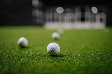 Indoor golf scene featuring multiple white golf balls on artificial grass, with blurred background elements creating a dynamic sports atmosphere