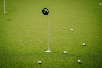 Indoor golf putting green with multiple white golf balls and flag, showcasing vibrant artificial turf and engaging recreational atmosphere
