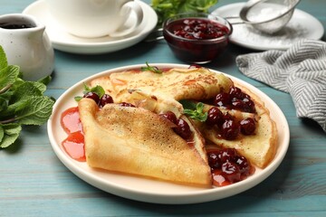 Delicious crepes with cherry jam served on light wooden table, closeup