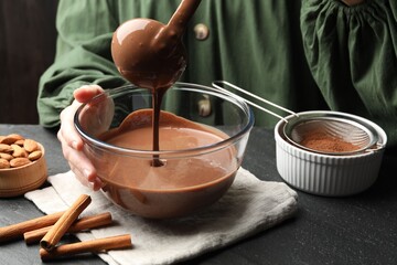 Woman taking liquid chocolate dough ladle at black table, closeup