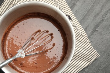 Liquid chocolate dough in bowl and whisk on black table, top view. Space for text