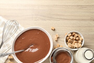 Liquid chocolate dough in bowl, cocoa powder, brown sugar and milk on wooden table, flat lay. Space for text