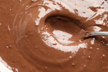 Liquid chocolate dough and spoon as background, top view